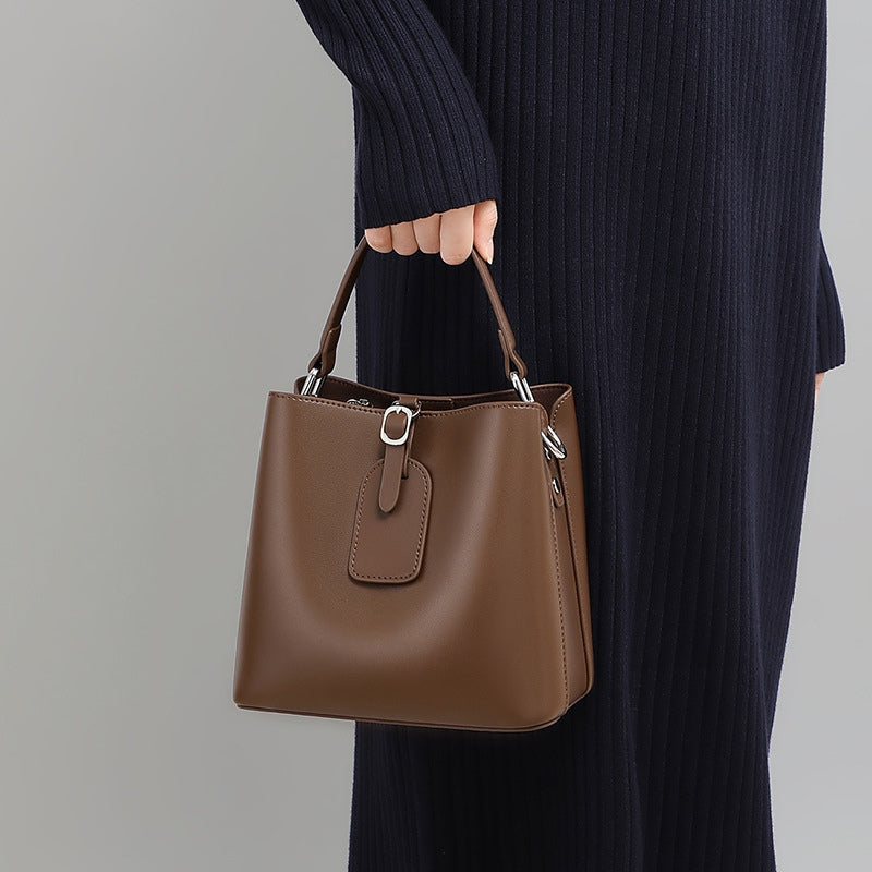 Woman carrying small leather bucket bag by top handle, brown