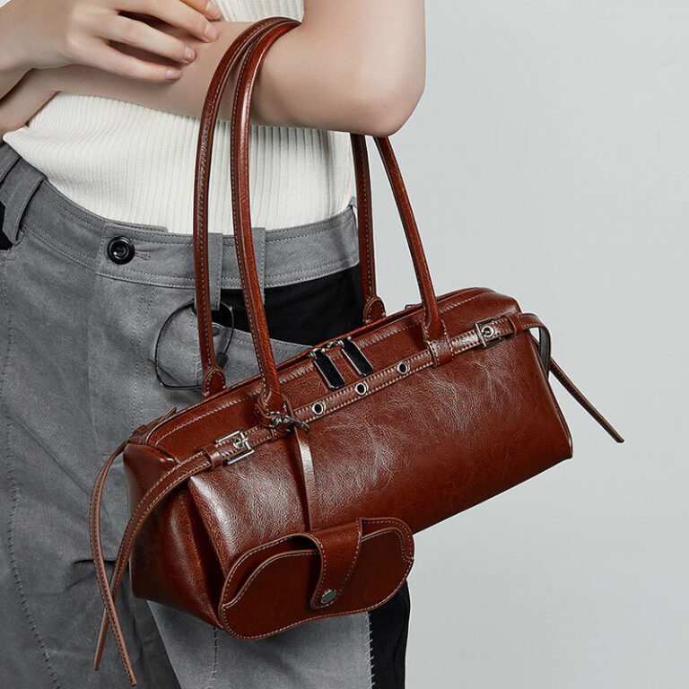 Brown leather handbag held by a person against a neutral background