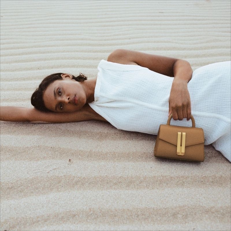 woman holding leather baguette bag crossbody in neutral outfit